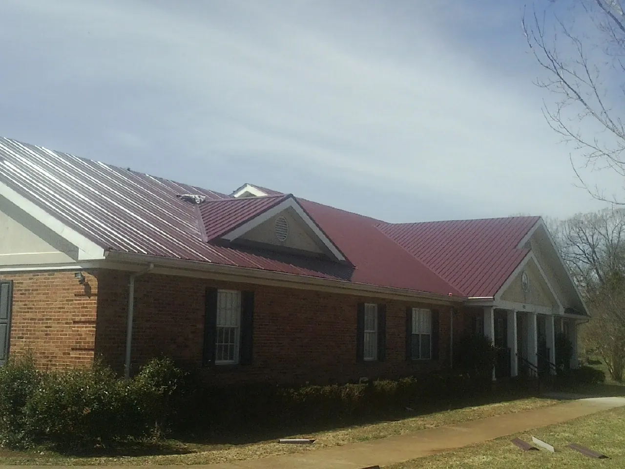 Red metal roof with gabled entries on a long brick building, from a Hail Damage Roof Repair job in La Grange Park