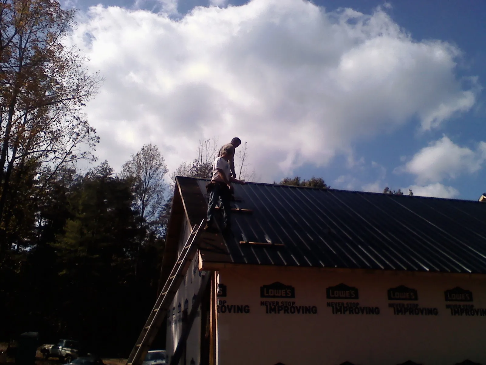 Roofer fastening dark metal panels high against a cloudy sky, from a Roof Inspection job in La Grange Park