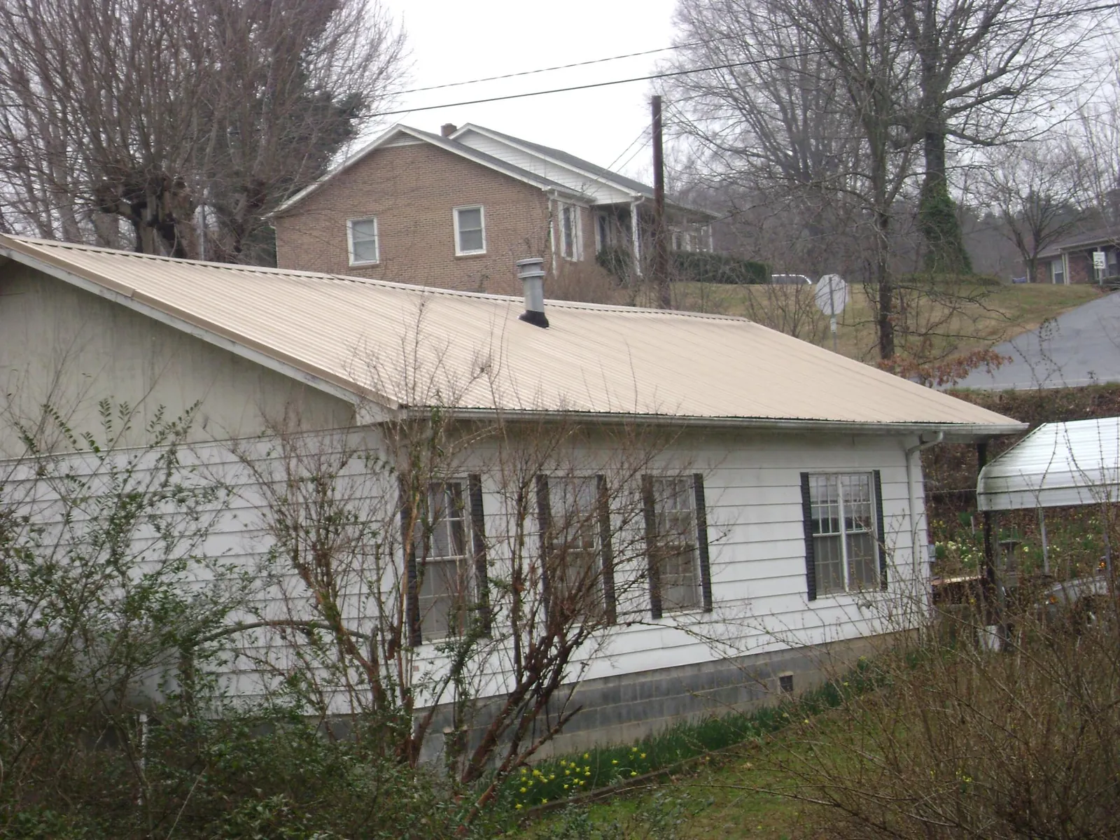 Tan metal roof on a white sided house set into a hillside — Commercial Roofing by Roofing Brothers in La Grange Park